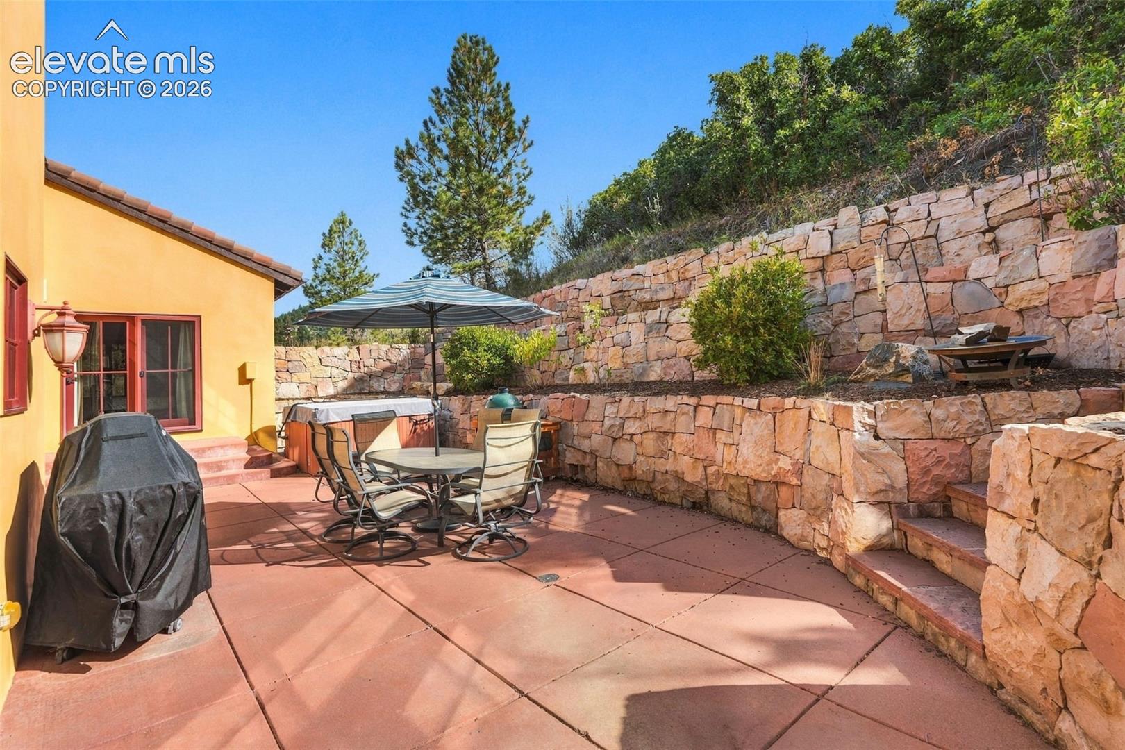 Spacious concrete patio with a built-in spa, tiered stone retaining walls, and integrated stone steps