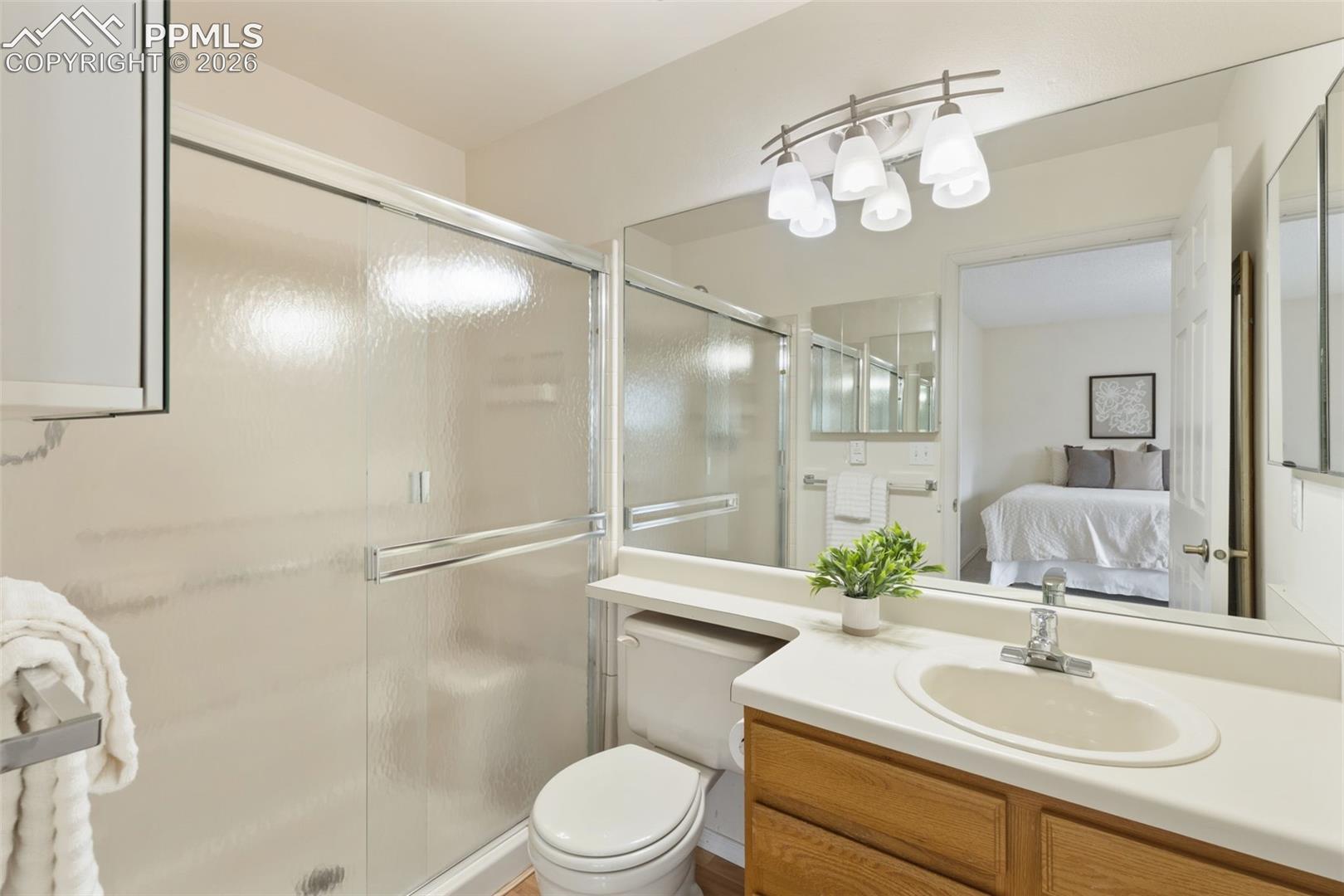 Bathroom featuring a shower with sliding glass doors, a vanity with a light countertop and wood cabinetry, and a mirrored wall