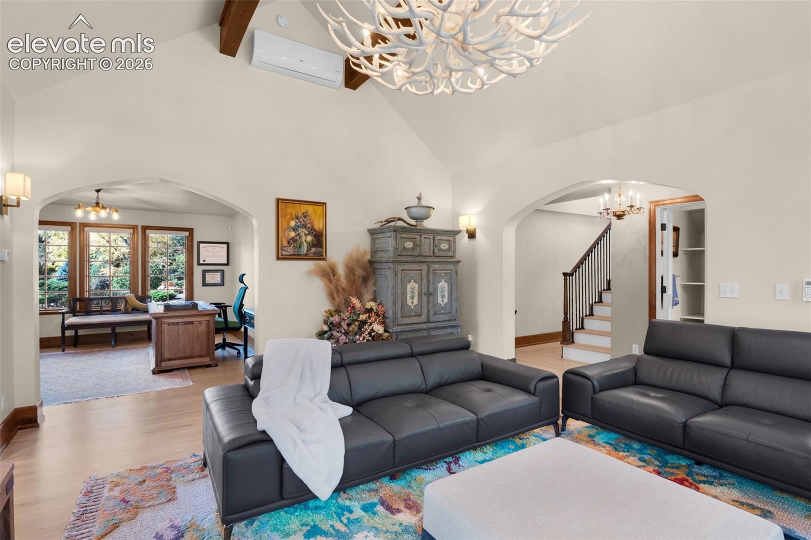 Vaulted ceilings with exposed wood beams, arched doorways, expansive wood-finish flooring, and a decorative antler chandelier