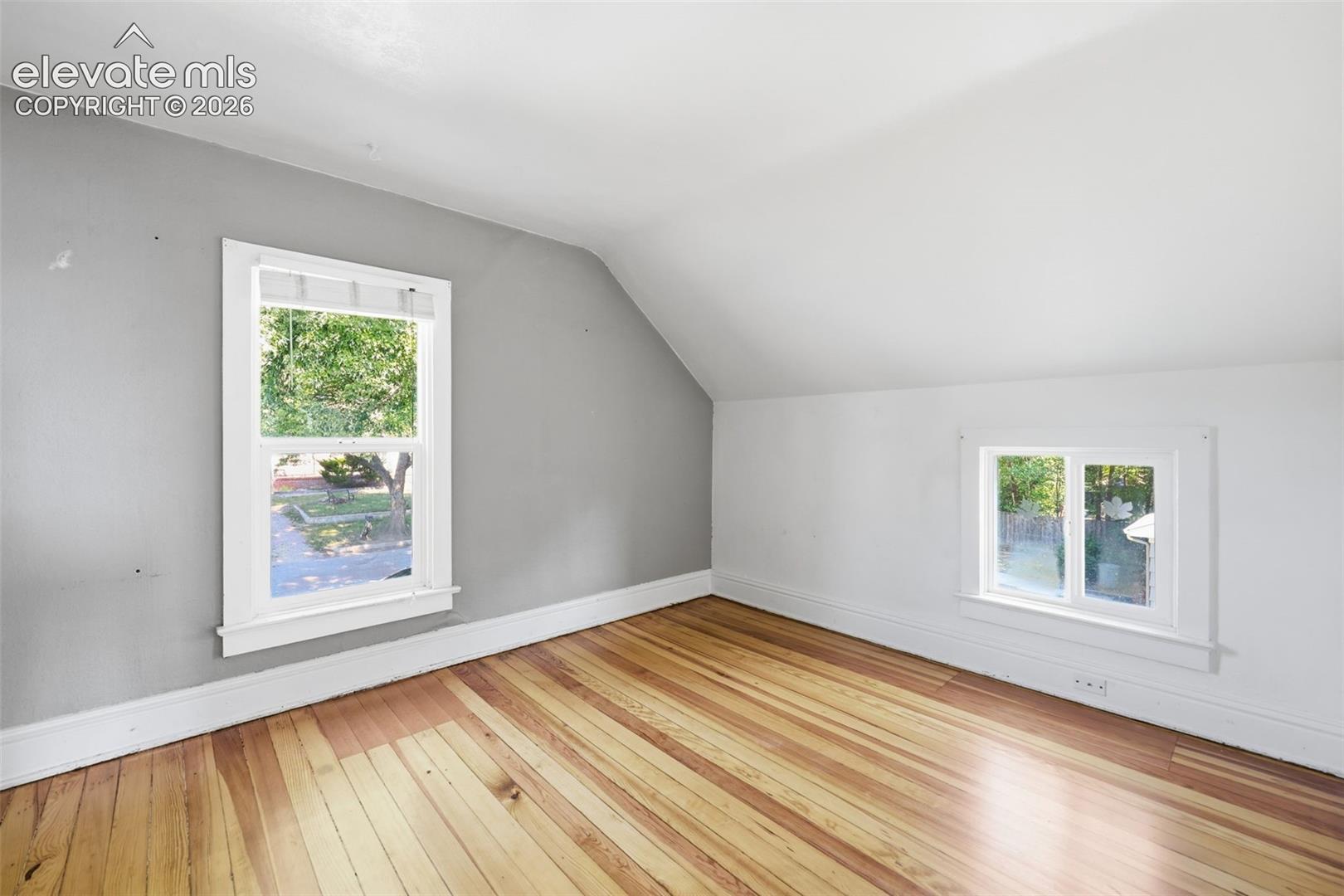Secondary upper bedroom with pine hardwood flooring, sloped ceiling, and a large and small window.