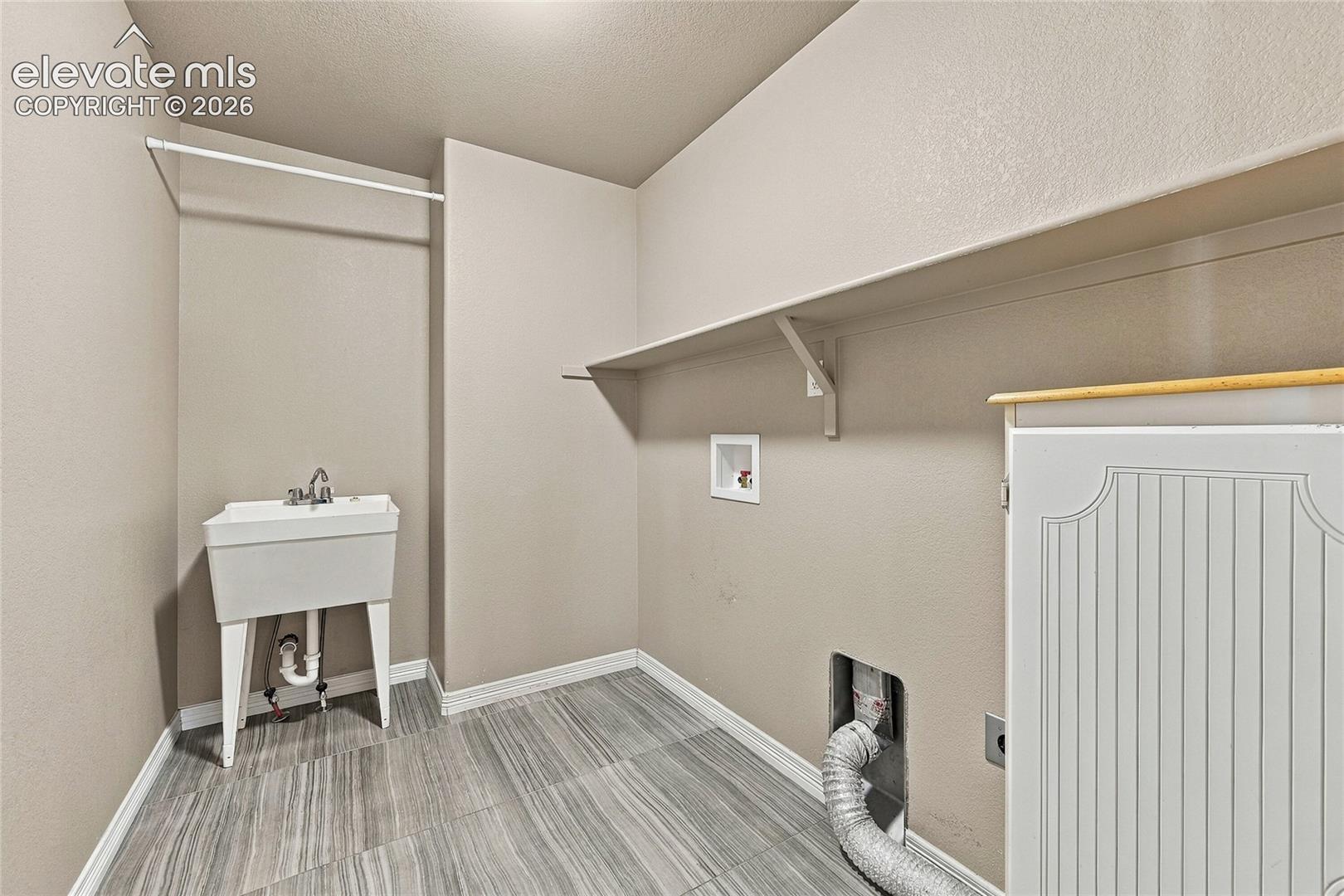 Utility space featuring neutral walls, wood-finish flooring, a wall-mounted shelf, a utility sink, and dedicated appliance connections
