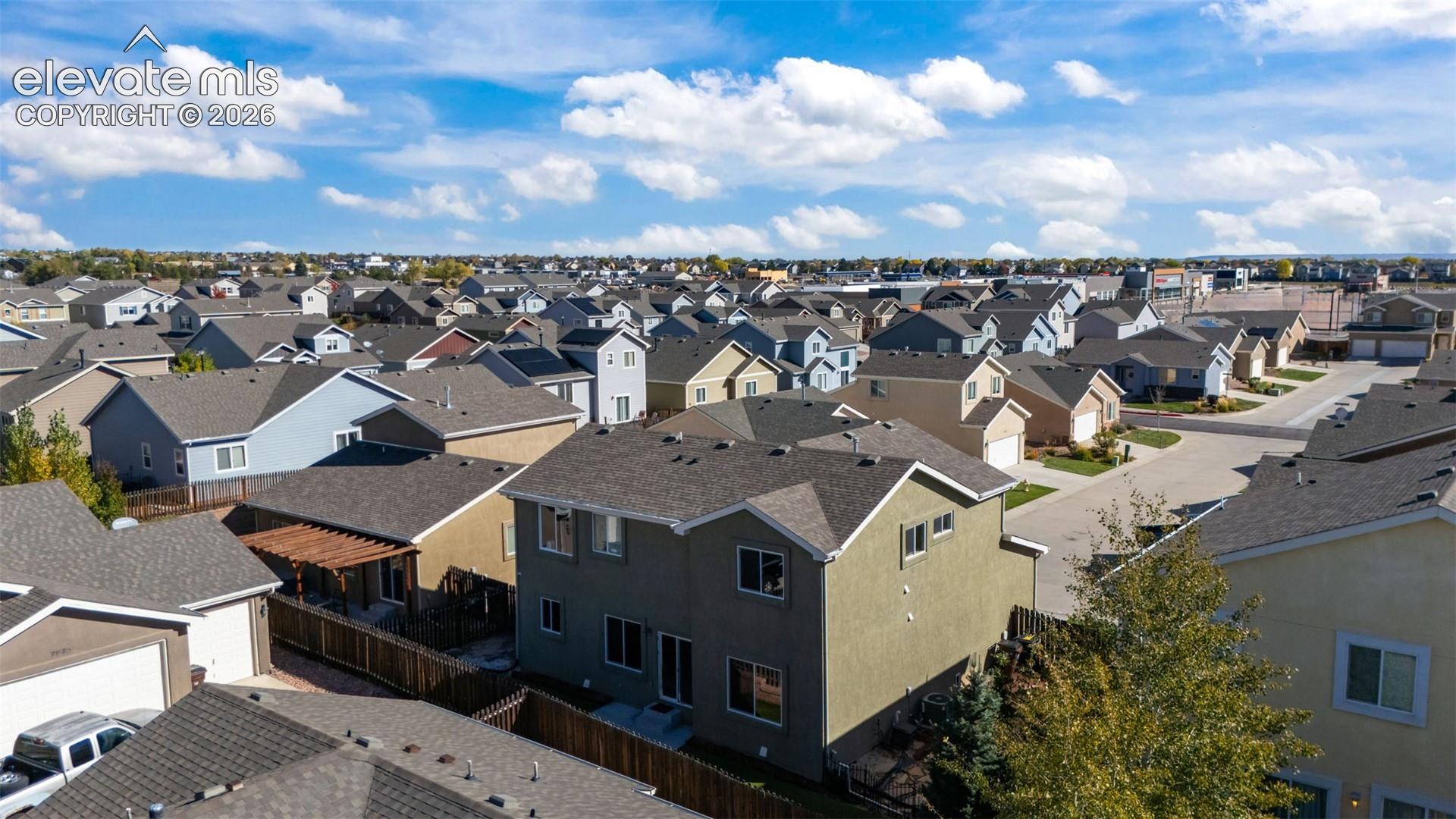 Aerial perspective of a multi-story residence featuring a composite shingle roof, stucco exterior, rear-facing wood pergola, and wood privacy fencing