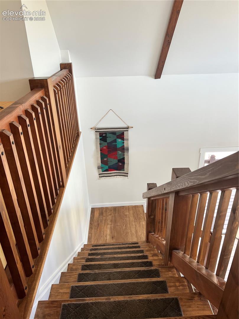 Hardwood staircase with integrated runners, wood-finish flooring, wood railing, and exposed ceiling beam