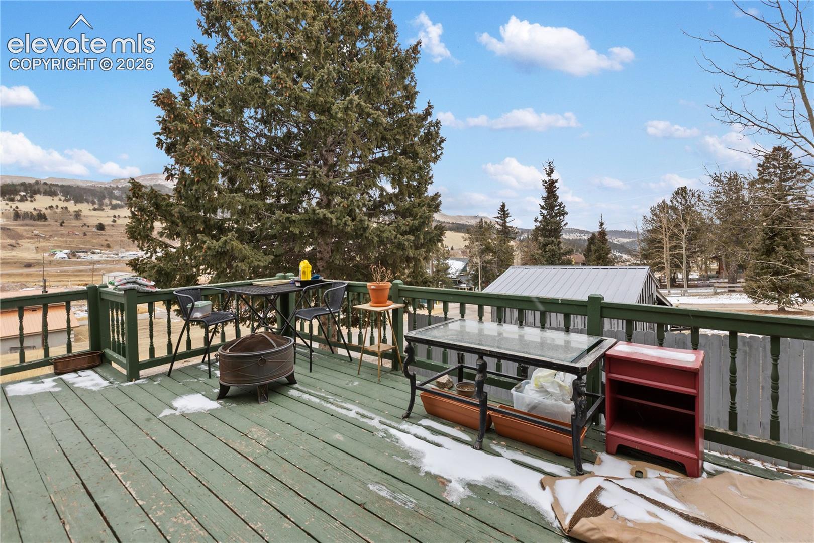 Raised outdoor deck featuring painted wood-finish planking, matching spindle railings, and mountain terrain backdrop
