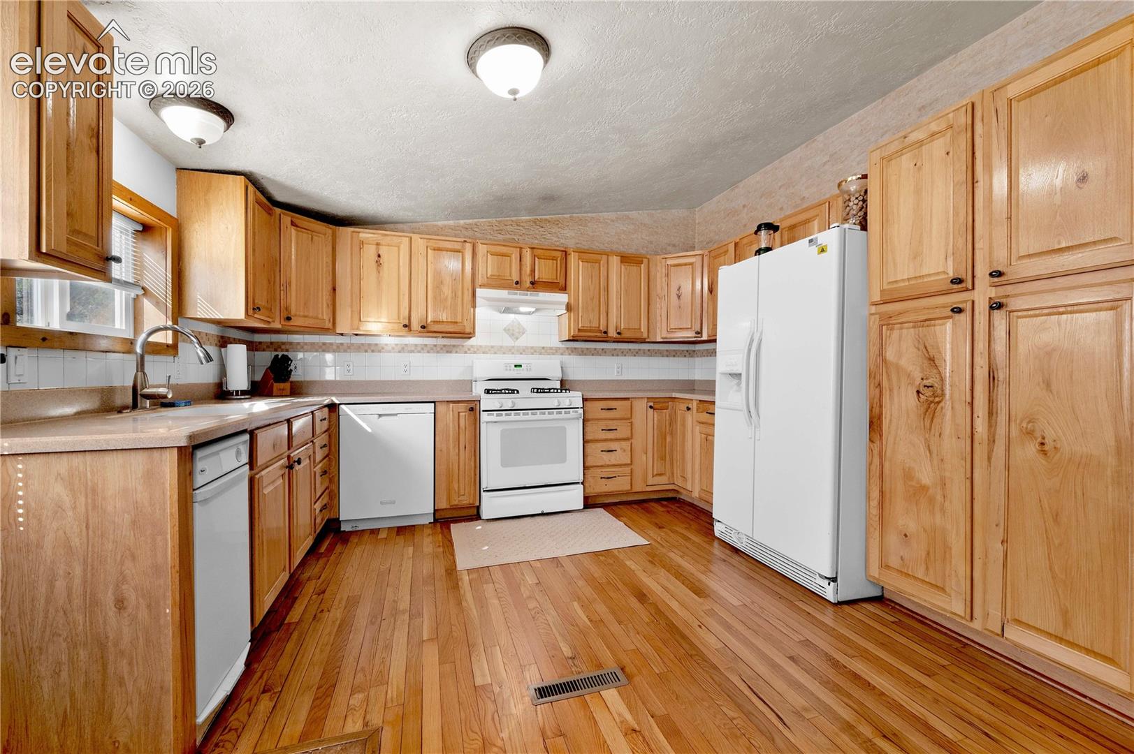 Kitchen featuring a textured ceiling, sink, light wood-type flooring, and white appliances