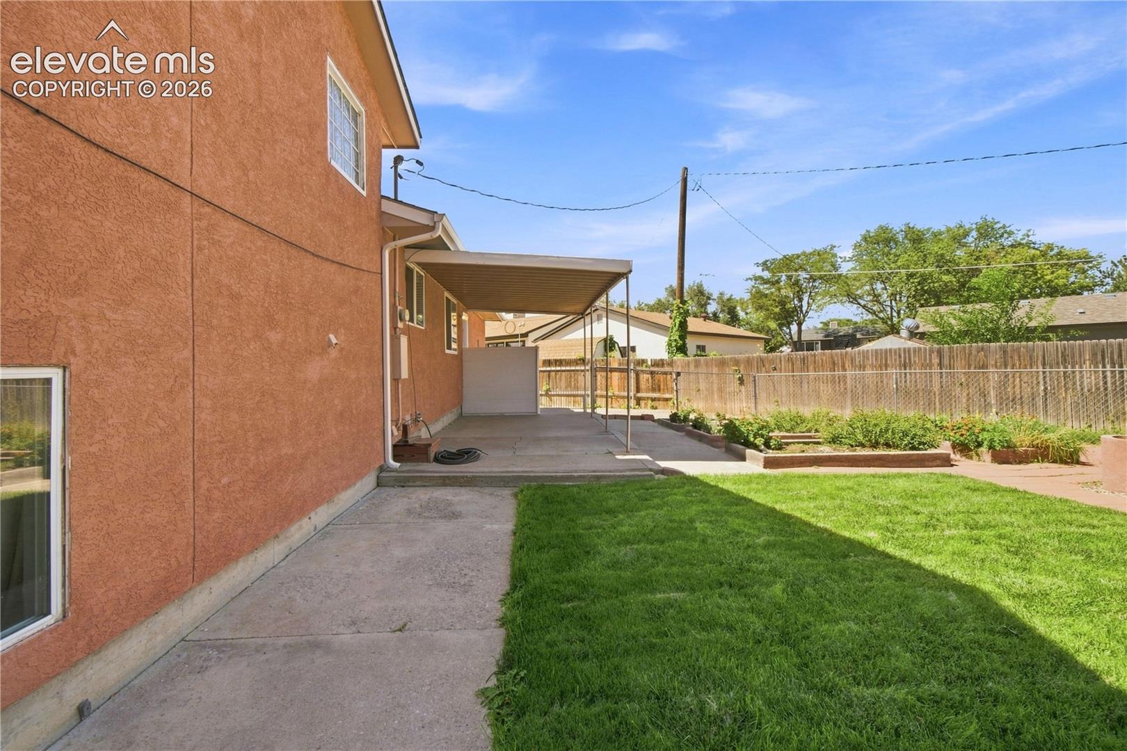 Stucco exterior, covered concrete patio, concrete pathway, fenced yard, and raised garden beds