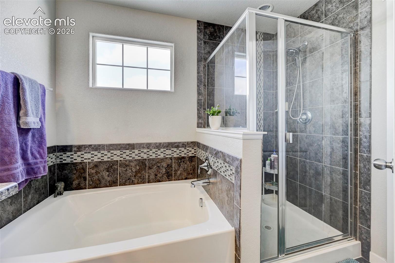 Soaking tub with a tile surround, glass-enclosed shower, mosaic tile accent banding, and a rectangular multi-pane window