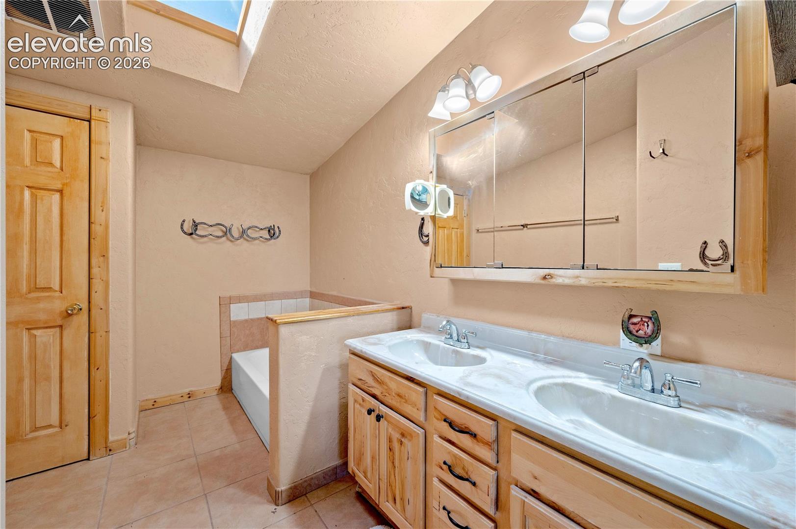 Bathroom with tile patterned floors, a bathtub, vanity, a textured ceiling, and a skylight