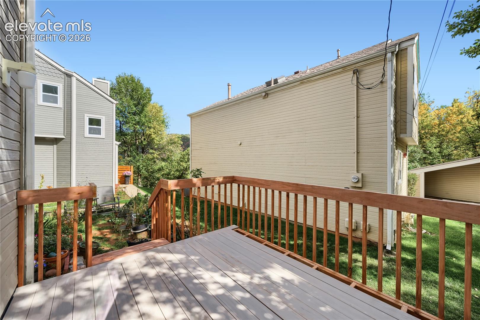 Spacious composite deck featuring wood-finish railings and multiple levels, overlooking a verdant backyard with mature tree coverage