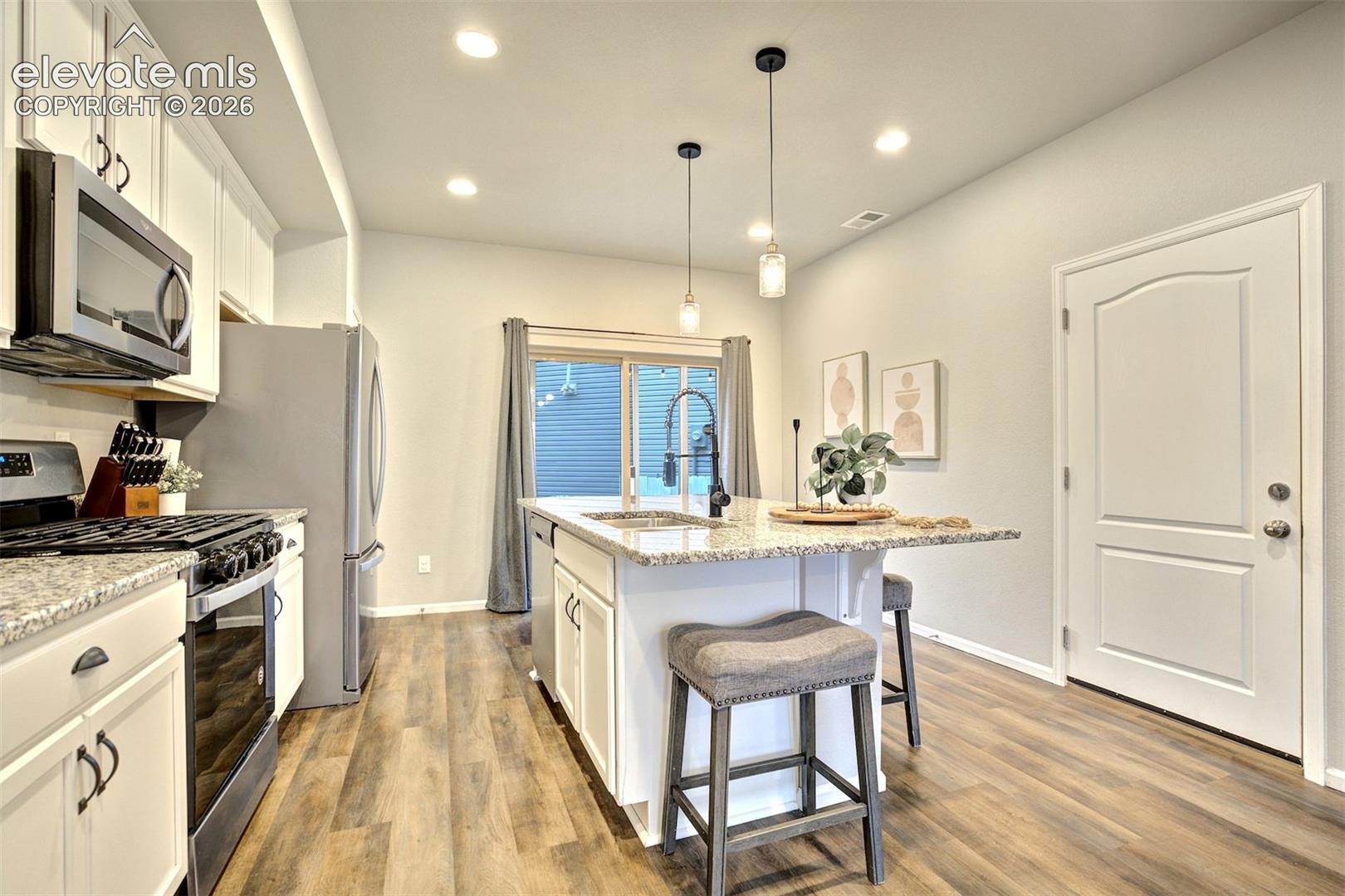 Kitchen featuring white shaker-style cabinetry, stone-finish countertops, stainless steel appliances, wood-finish flooring, and recessed lighting