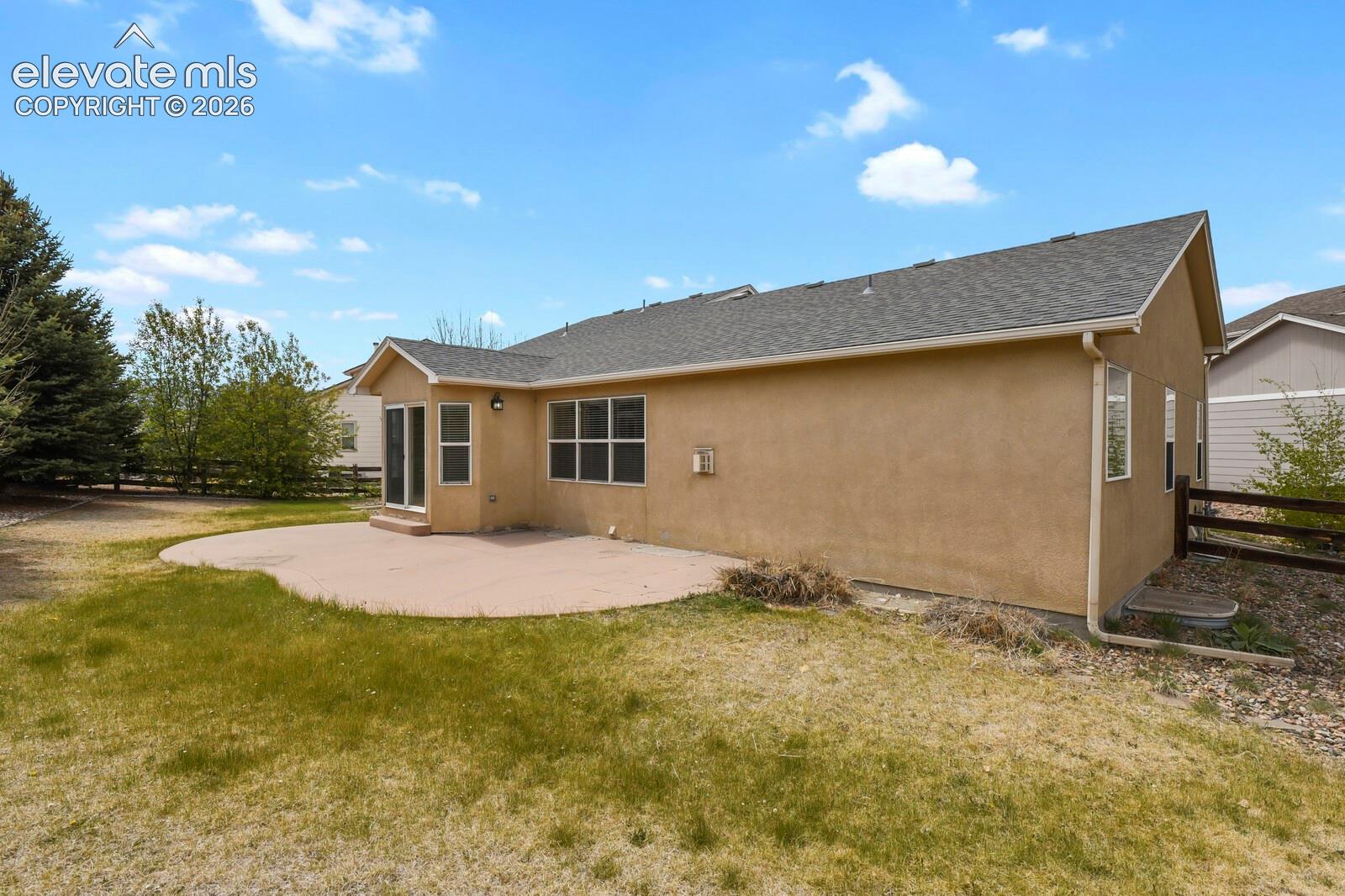 Expansive backyard featuring a curved concrete patio, stucco exterior, multiple windows, and a wood fence