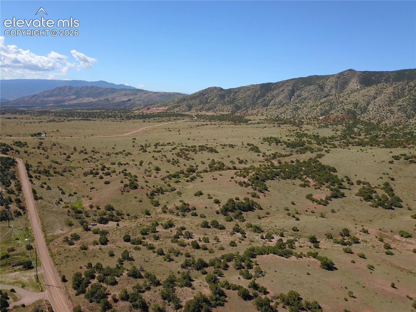 Expansive open land with distant mountains, a dirt road, and scattered low-lying natural shrubbery