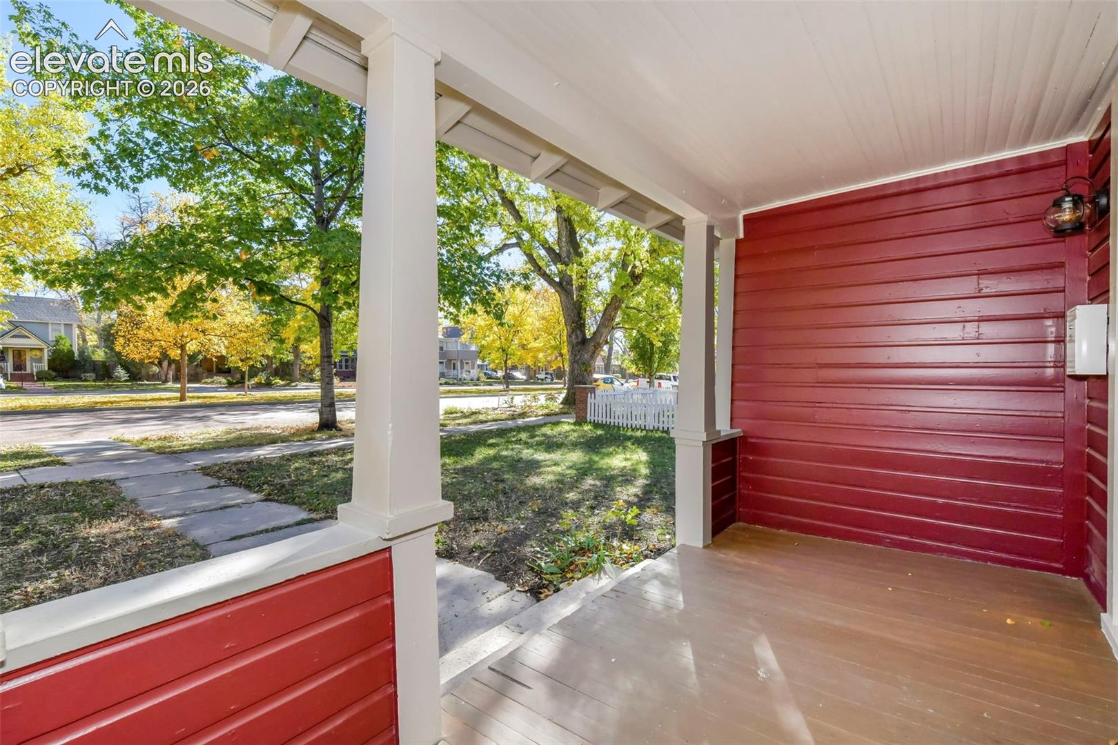 Covered front porch featuring wood-plank flooring, lap siding, structural columns, and a wall-mounted light fixture