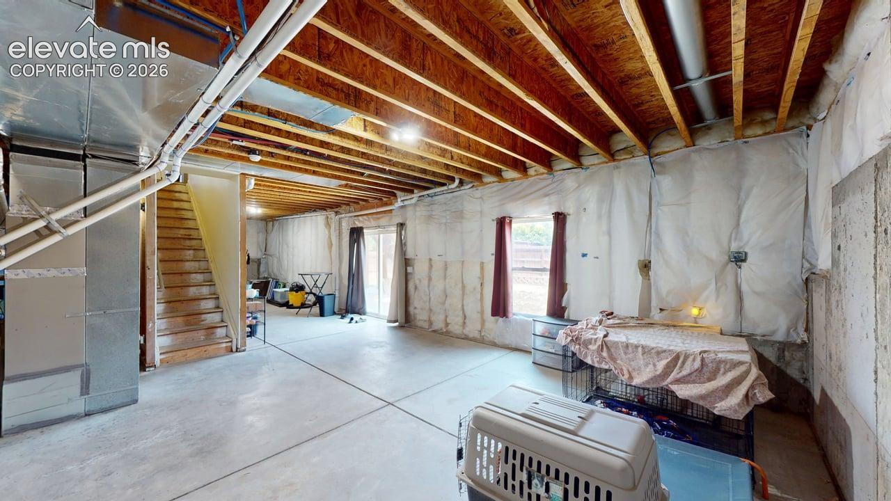 Expansive unfinished basement featuring exposed ceiling joists, concrete flooring, and a walk-out sliding door