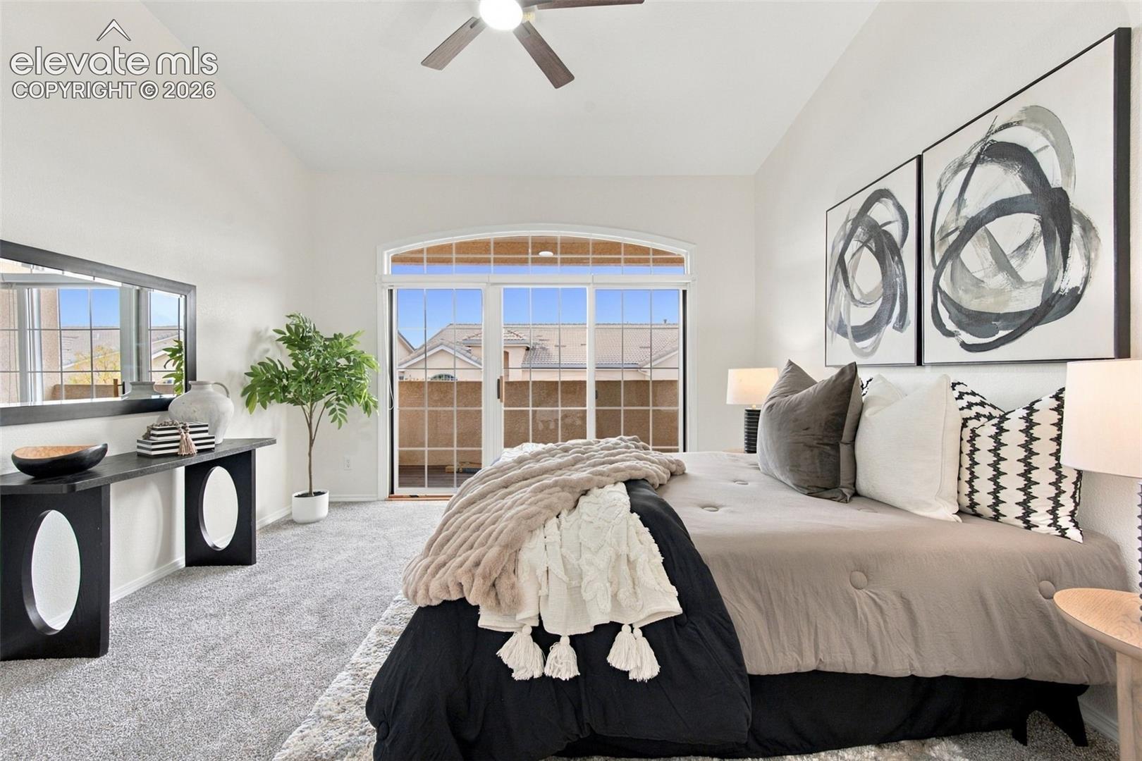 High-ceilinged room with neutral wall-to-wall carpeting, ceiling fan, and sliding glass door featuring an arched transom window