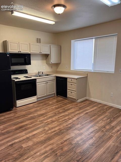 Kitchen featuring wood-finish flooring, white cabinetry, solid-surface countertops, and a full suite of black appliances
