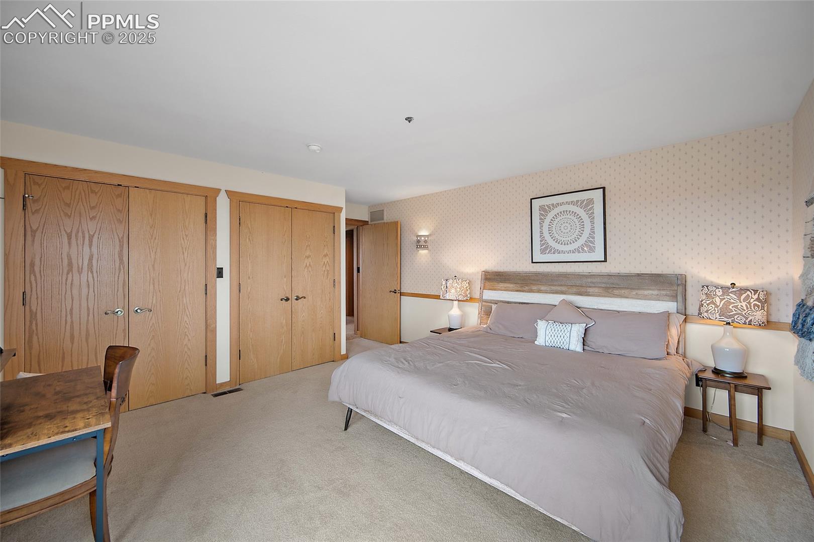 Carpeted bedroom featuring wallpapered walls and two closets