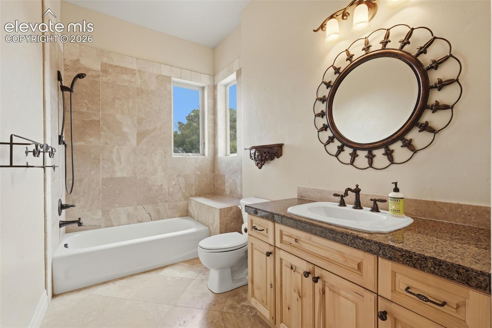 Bathroom featuring a light-toned tile floor, a built-in tub with dark bronze fixtures, and a tiled shower surround