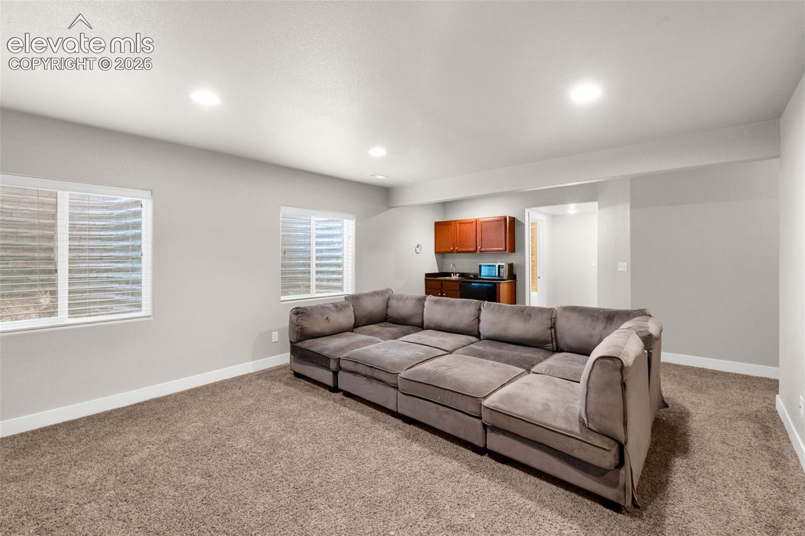 Neutral-toned interior space featuring recessed ceiling lighting, two egress windows with window wells, and a kitchenette area with wood cabinetry and countertop
