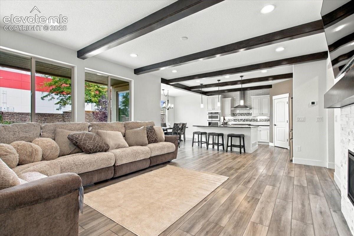 Open-concept interior featuring wood-finish flooring, exposed ceiling beams, large windows, recessed lighting, and a kitchen with an island