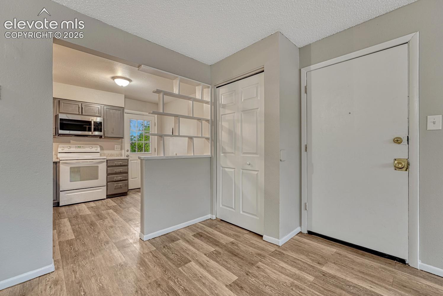 Wood-finish flooring, white paneled entry door, built-in shelving unit, white bi-fold closet doors, and a ceiling-mounted light fixture