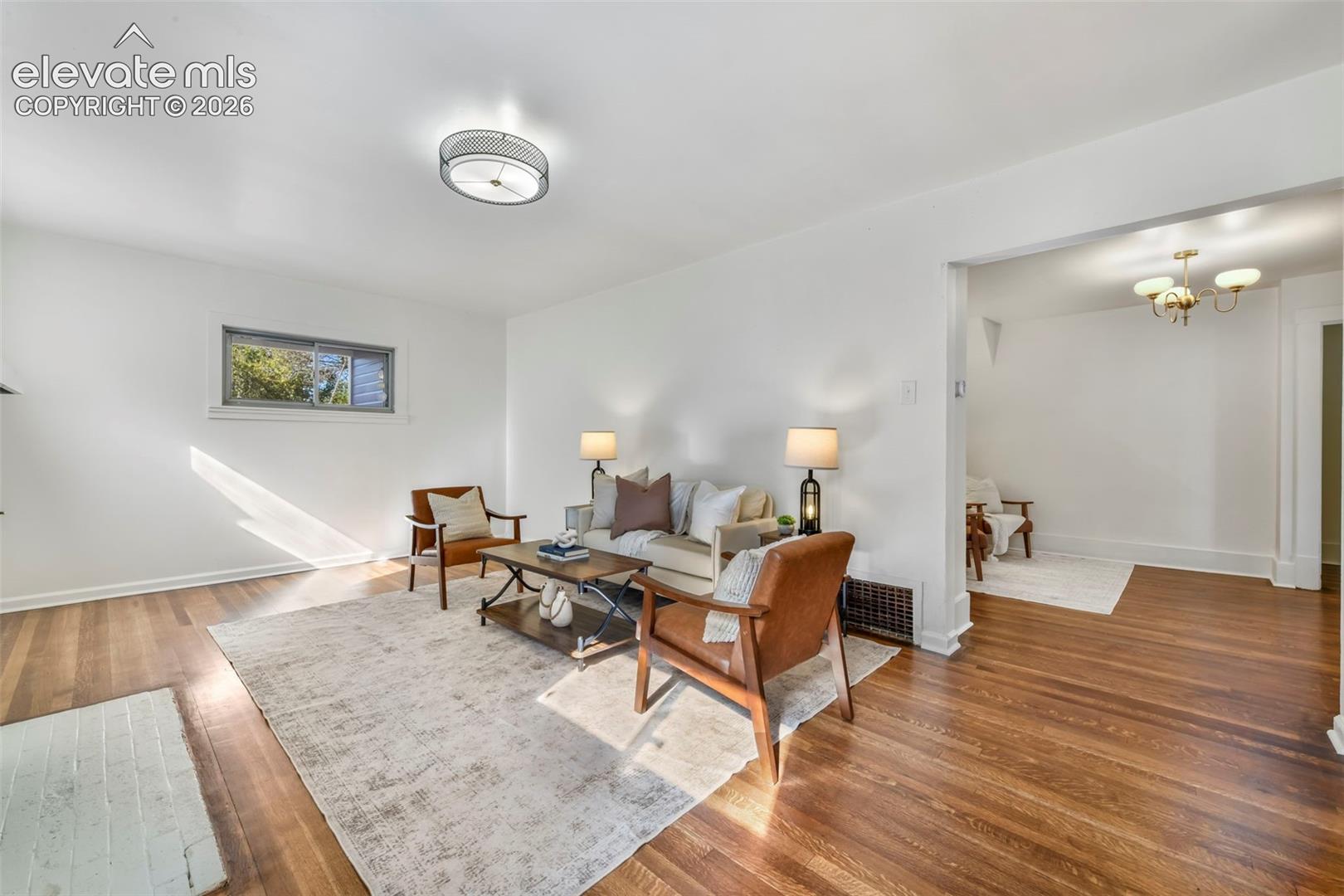 Living area featuring wood-finish flooring, a painted brick fireplace hearth, a drum-style ceiling light fixture, and a multi-arm chandelier