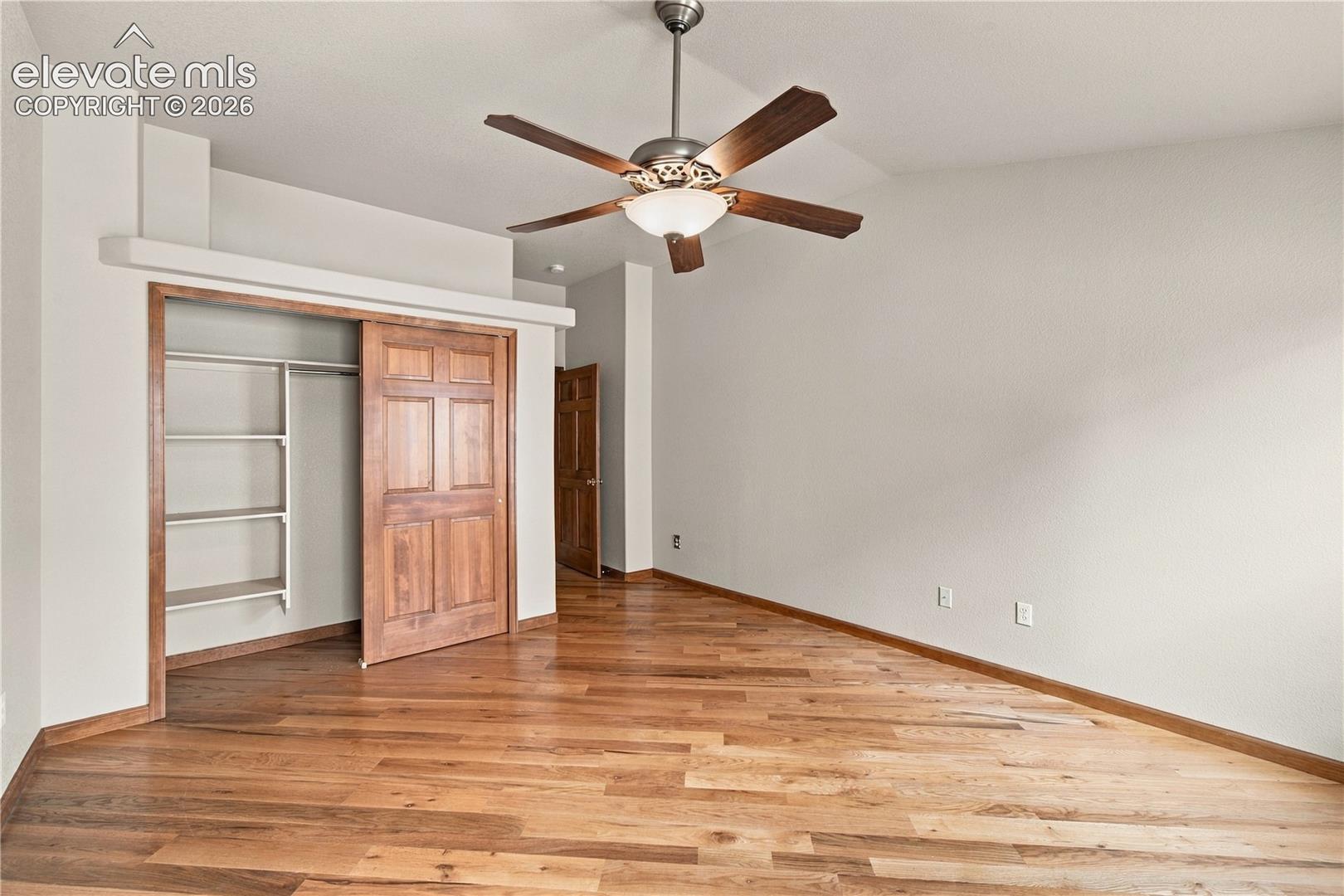 Room featuring wood-finish flooring, a ceiling fan with integrated lighting, a closet with a wooden sliding door and built-in shelving, and a six-panel wooden interior door