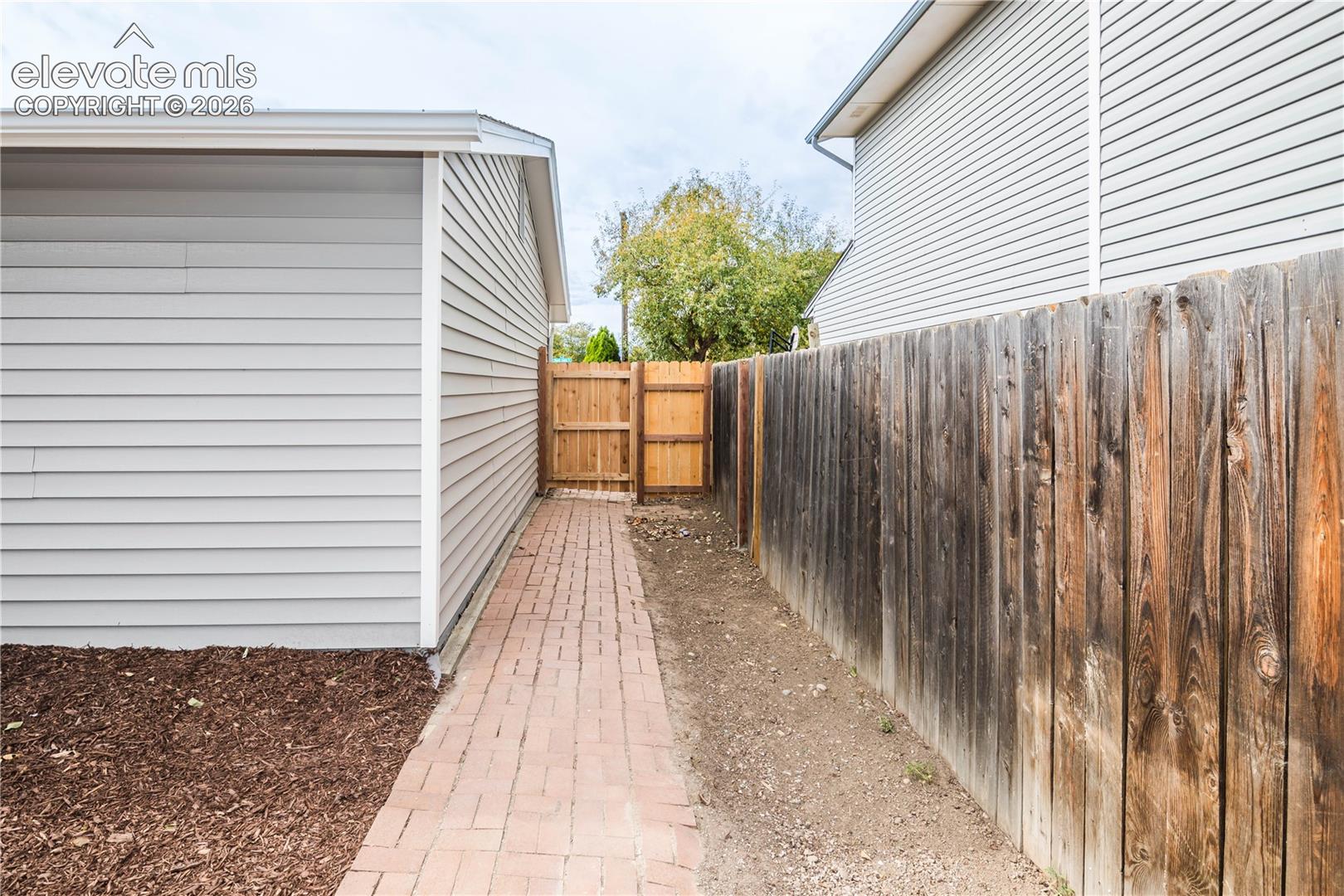 Exterior side yard featuring horizontal siding, a red brick paver walkway, and a full-height vertical wood privacy fence with a matching gate