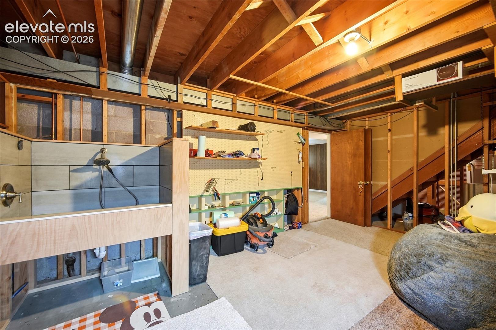 Utility area featuring a custom plywood utility station with a tile-surround wash basin, exposed wood-joist ceiling, and wood staircase