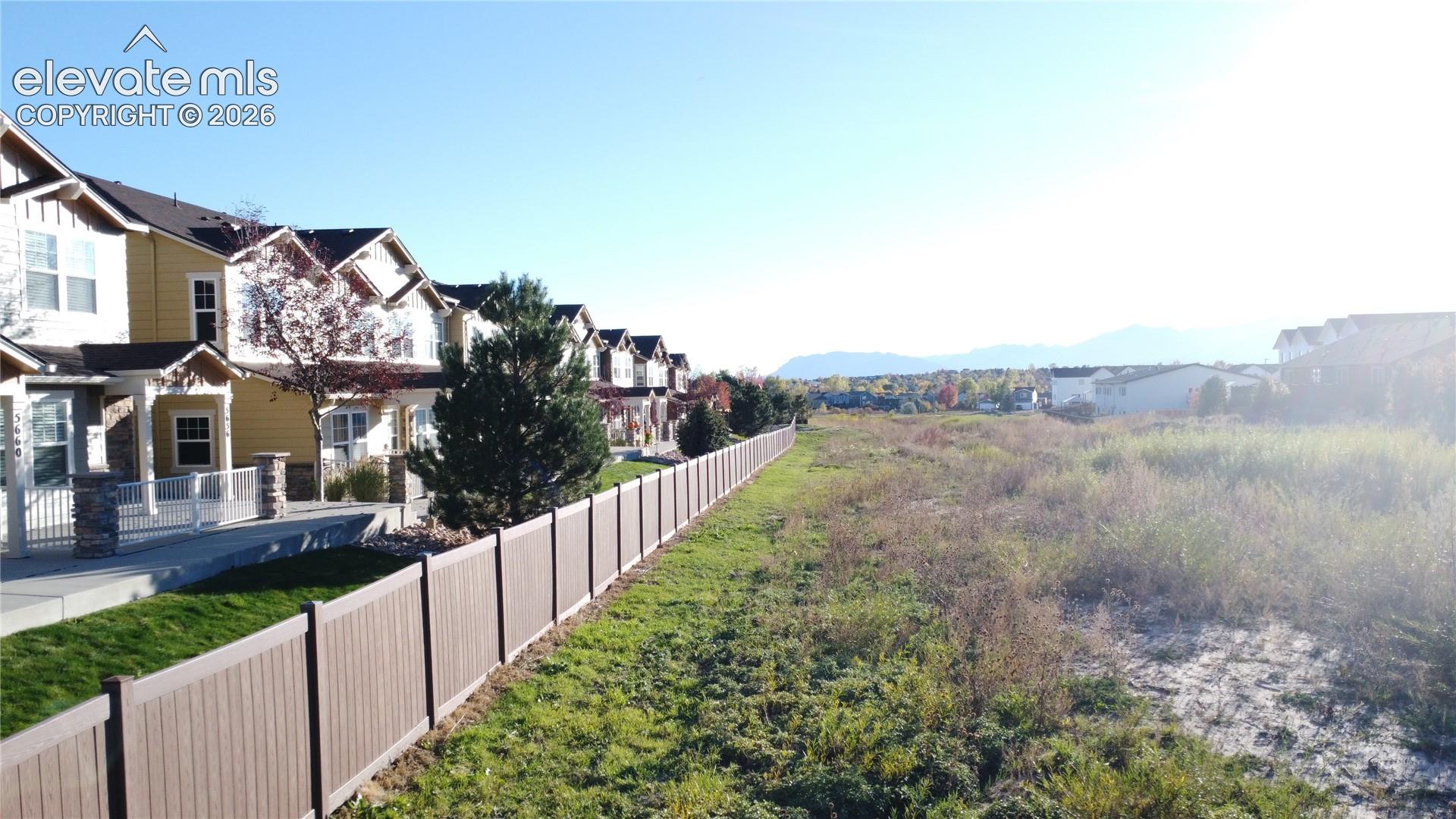 Multi-level residential exterior featuring stone veneer accents, covered entryway, vinyl privacy fencing, and mountain backdrop