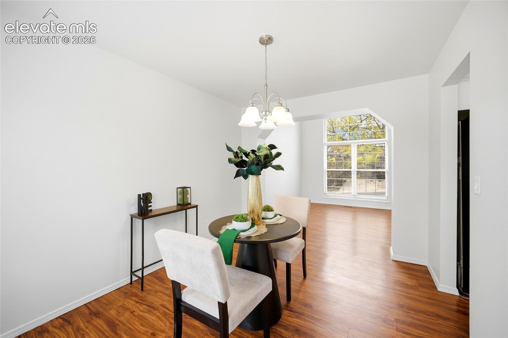 Open-concept area featuring wood-finish flooring, a three-light chandelier, and large windows with exterior greenery