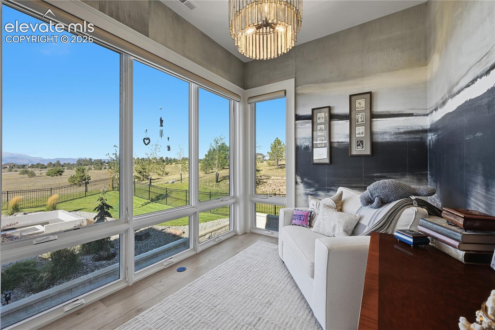 Floor-to-ceiling windows, wood-finish flooring, and tiered crystal chandelier featuring a metallic finish