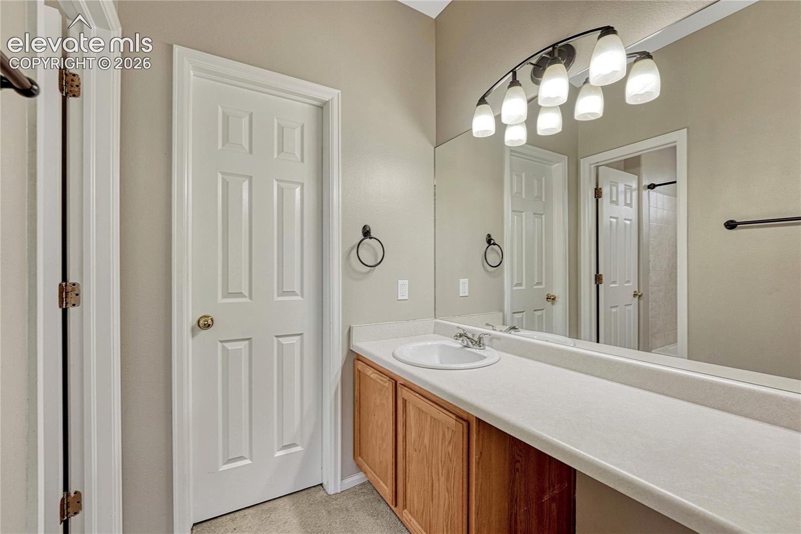 Bathroom vanity featuring natural wood cabinetry, integrated solid-surface countertop with an oval basin, a full-width wall mirror, and a multi-light overhead fixture