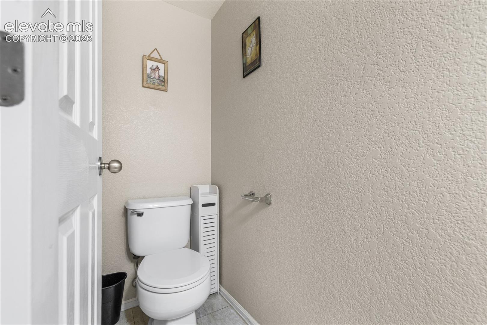 White ceramic commode, neutral-toned textured wall finish, and metal hardware
