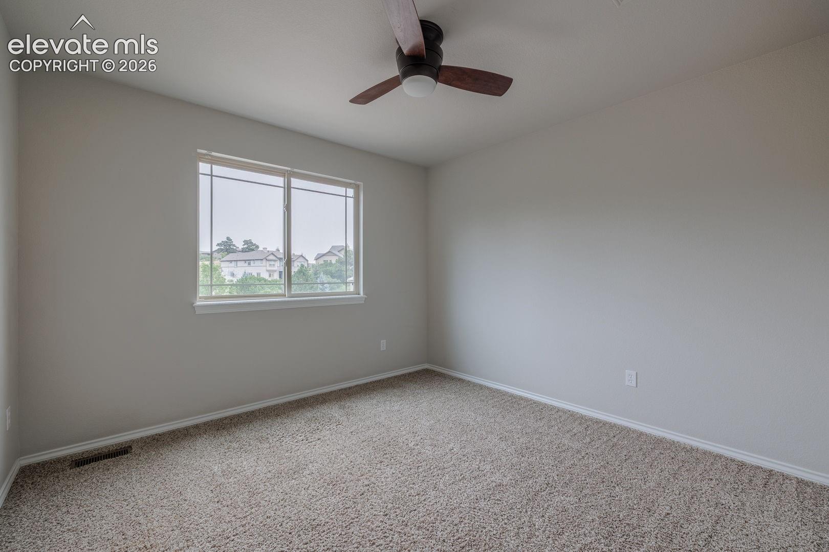 Spacious bedroom featuring neutral wall finishes, ceiling fan with dark finish, and abundant natural light from a large double-hung window