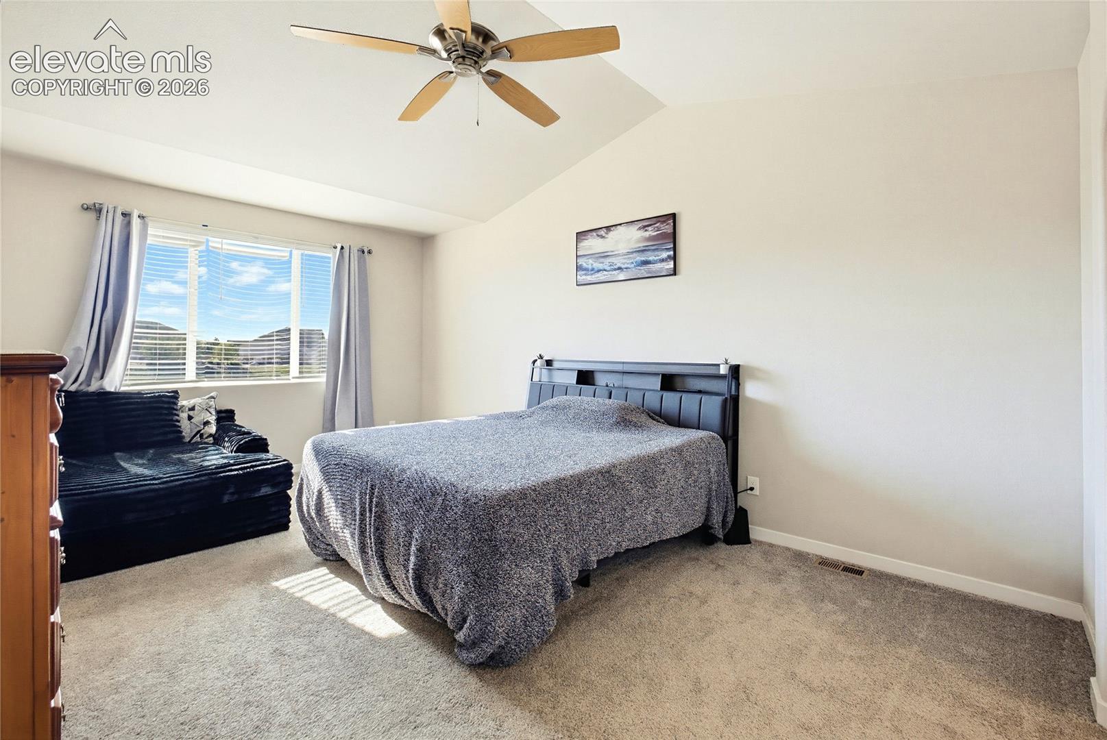 Vaulted ceilings featuring a central ceiling fan, carpeted flooring, and a window with horizontal blinds