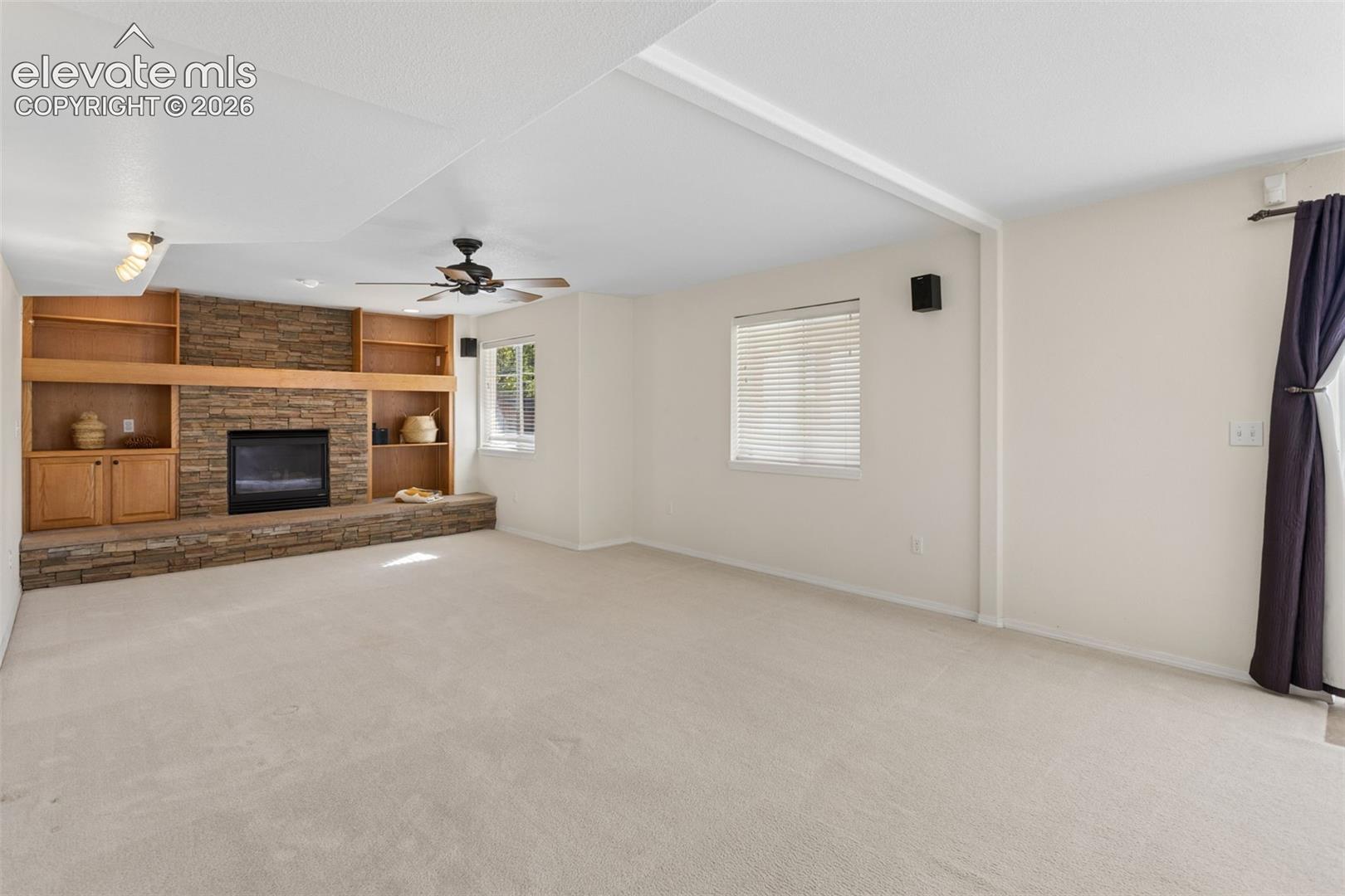Stone-faced fireplace with a raised hearth, built-in wooden cabinetry, recessed ceiling lighting, and a dual-blade ceiling fan