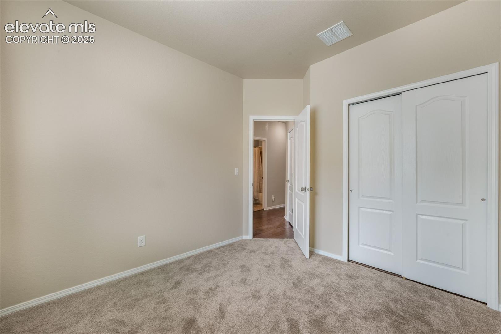 Neutral tone walls, beige carpeting, white trim, and white sliding closet doors