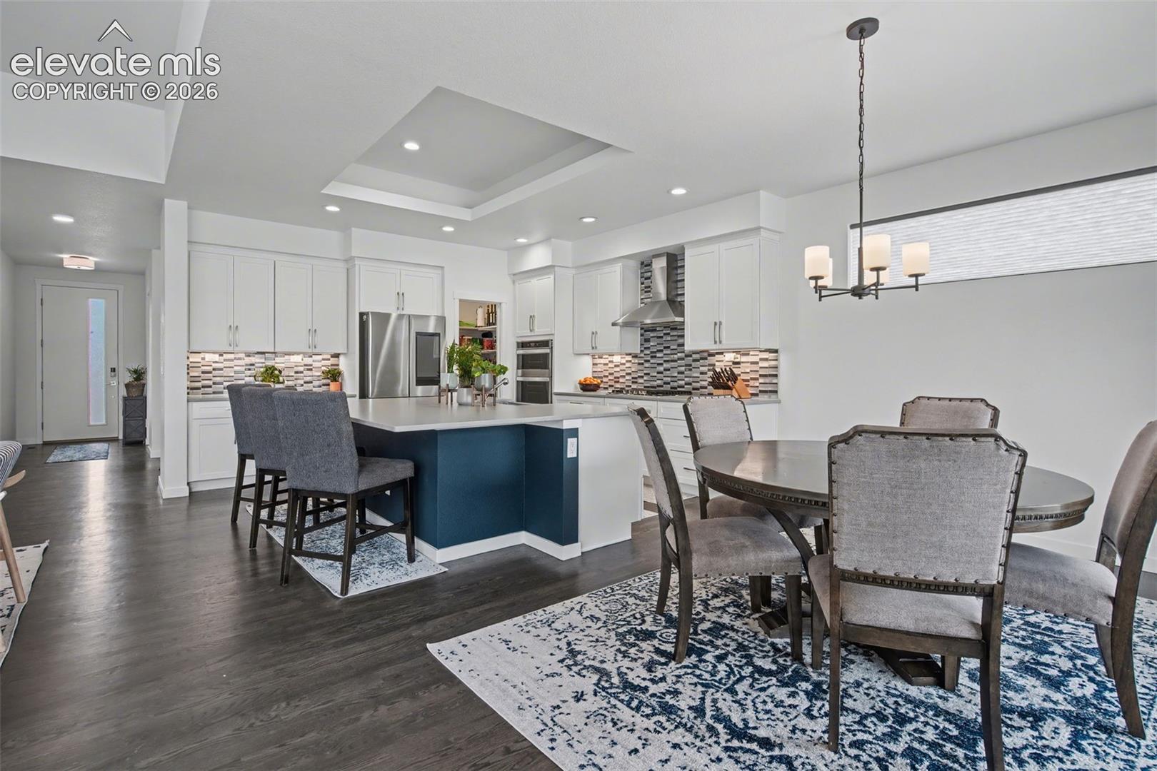 Dining room with a raised ceiling, dark wood-type flooring, and suspended lighting