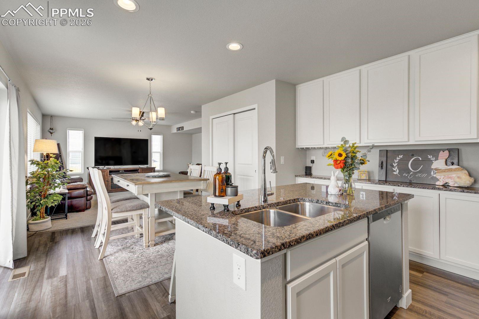 Kitchen with dark stone countertops, open floor plan, white cabinetry, an island with sink, and recessed lighting