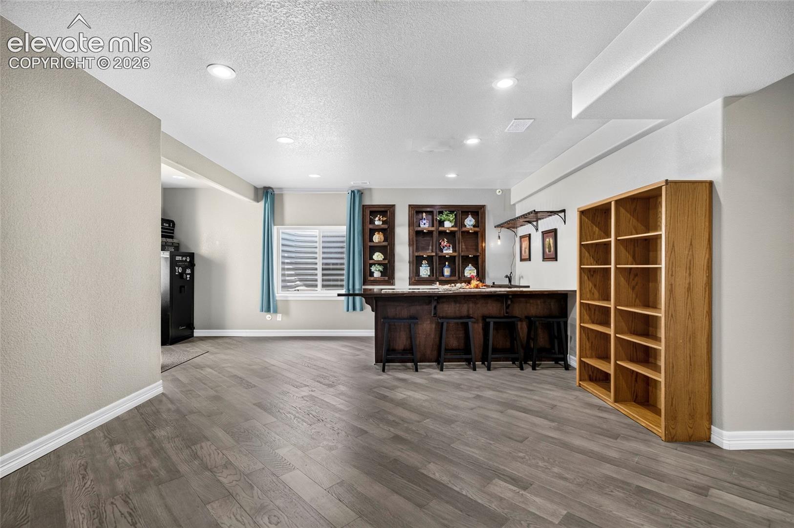 Finished recreation area featuring wood-finish flooring, recessed lighting, and a built-in wet bar with dark wood cabinetry and shelving