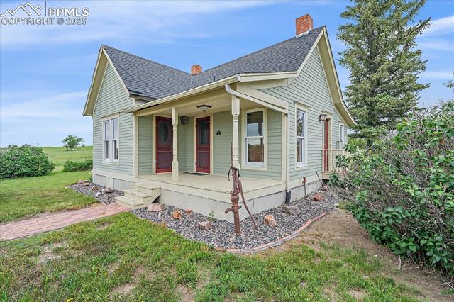 View of front of property with a porch, roof with shingles, a front yard, and a chimney