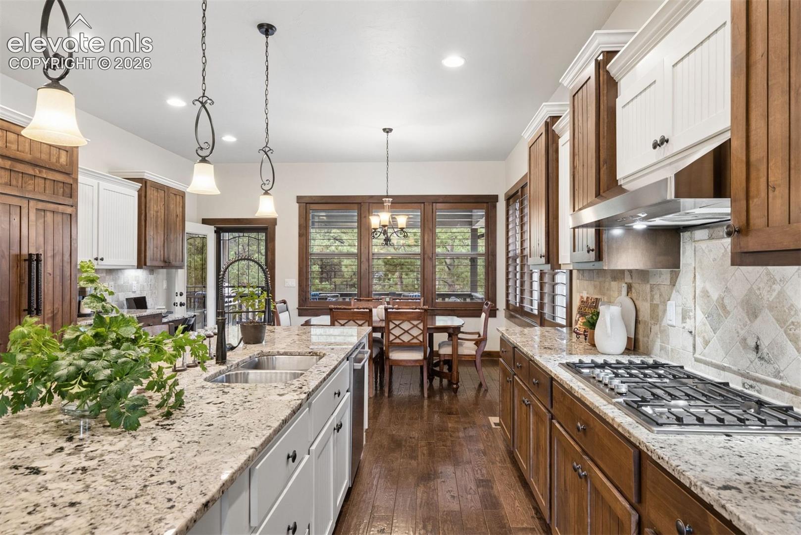 Kitchen featuring custom two-tone cabinetry, stone countertops, stainless steel gas cooktop, pendant lighting, and wood-finish flooring
