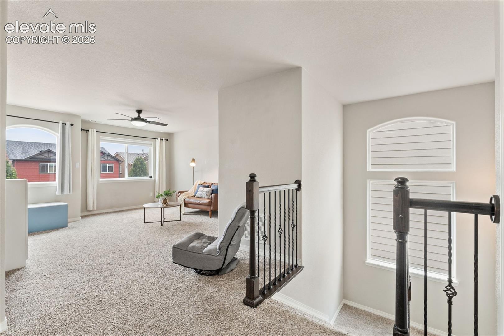 Carpeted loft area with multiple windows, a ceiling fan, and wrought iron balusters