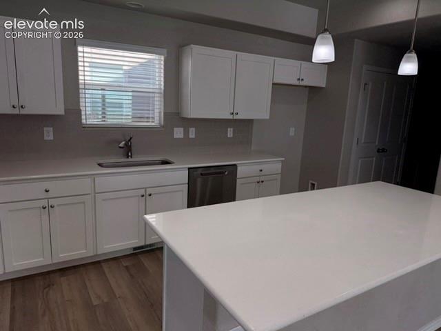 White shaker cabinetry, light-toned countertops, stainless steel dishwasher, wood-finish flooring, and pendant lighting fixtures