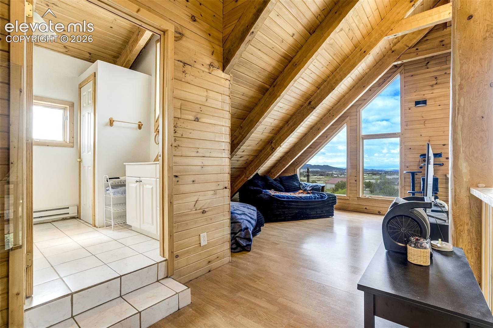Wood-paneled walls and ceiling beams complement a spacious room with wood-finish flooring