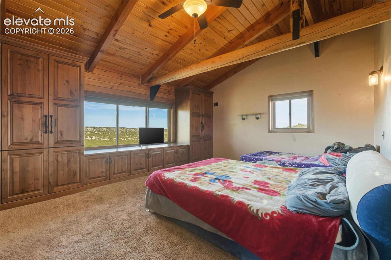 Vaulted wood-paneled ceiling with exposed beams, wood-finish built-in cabinetry, wall-mounted sconces, and a ceiling fan