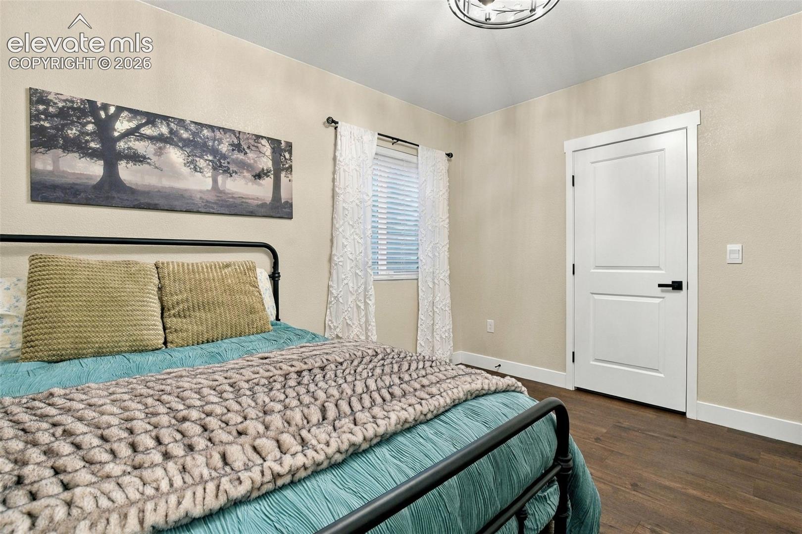 Wood-finish flooring, two-panel interior door with matte black hardware, multi-light flush mount ceiling fixture, and horizontal blind window treatment