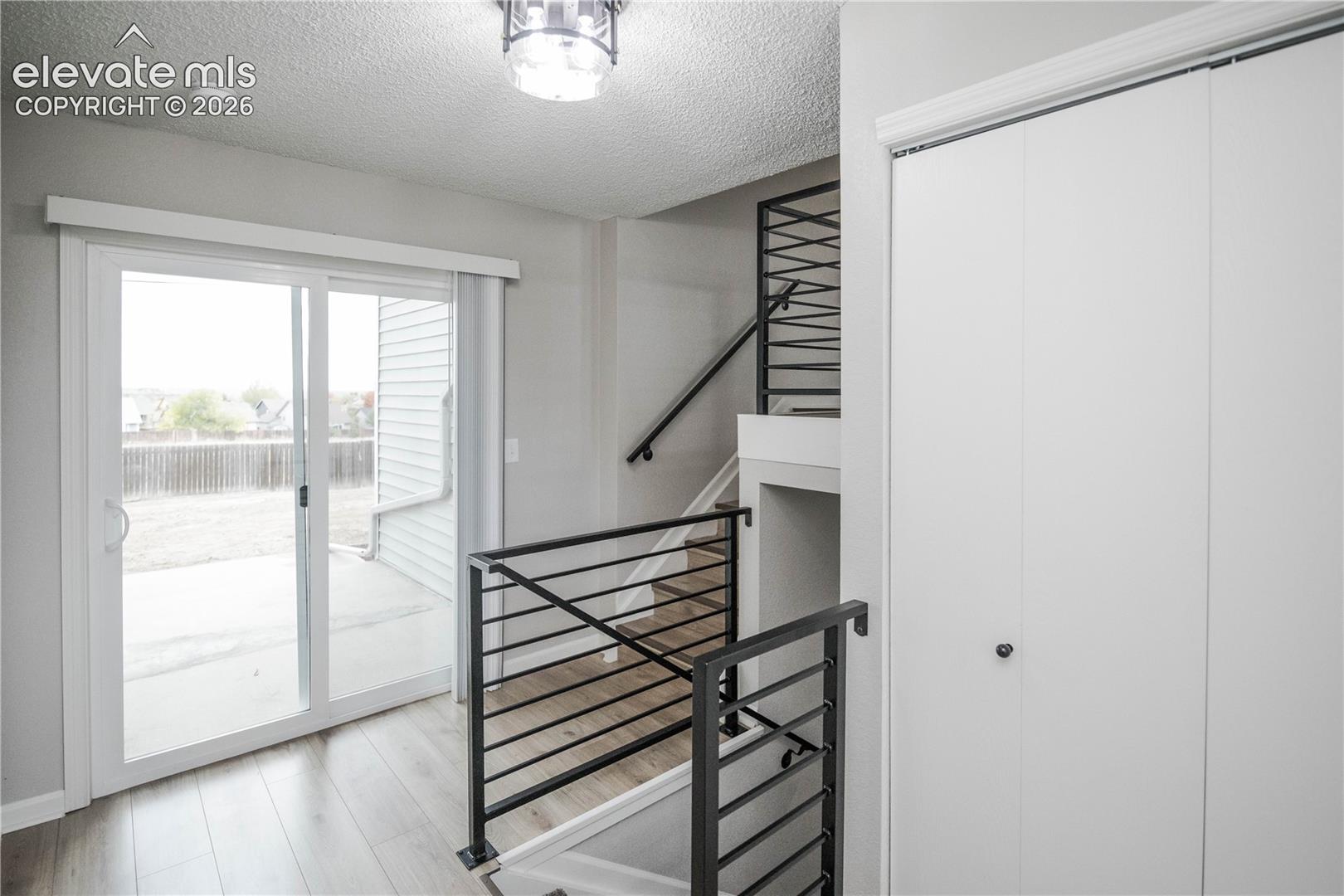 Sliding glass door, wood-finish flooring, matte black horizontal metal railing, and white bi-fold closet doors