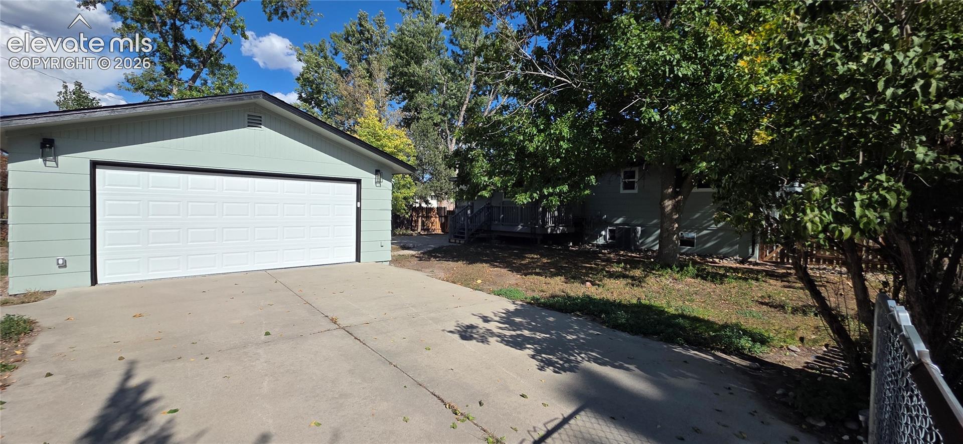 Detached garage with a large white panel door, concrete driveway, and exterior wall sconces